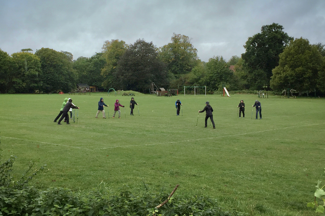 People socially distanced in a playing field learning Nordic Walking